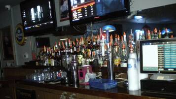 Zona de bar con varias televisiones mostrando deportes, una variedad de botellas de licores y un terminal de pago digital.