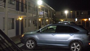 A parking lot with a silver car parked in front of a building with multiple balconies and exterior lights. - Wasco Inn Motel (Wasco)