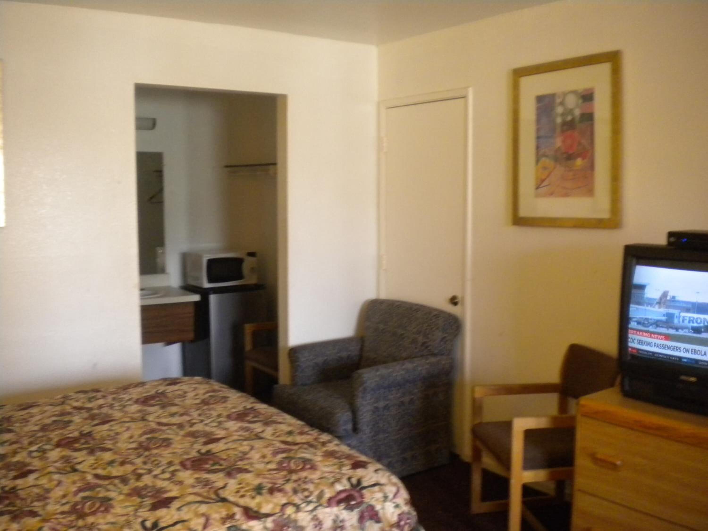 A bedroom with a bed, a chair, a television, and a microwave.