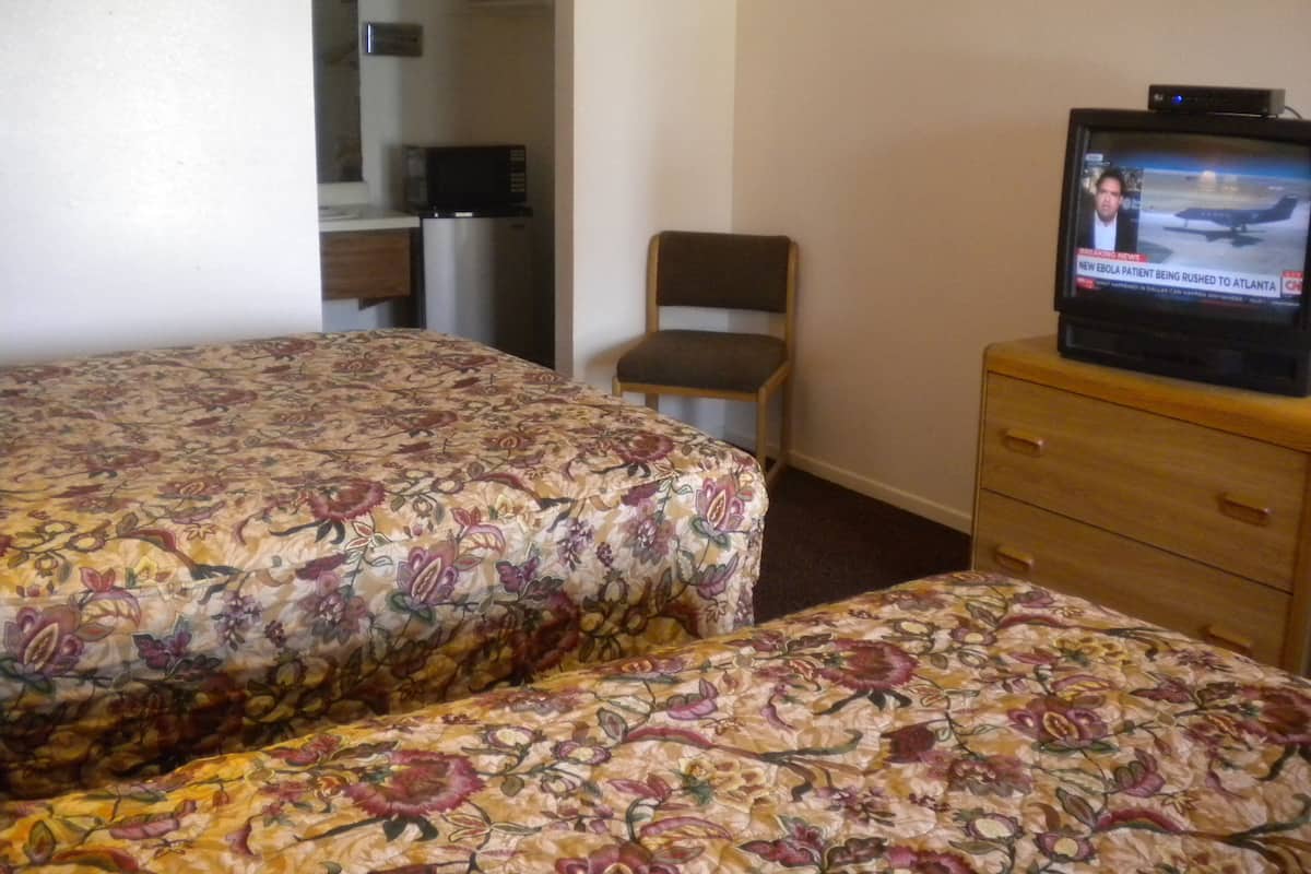Quarto de hotel com duas camas, televisão, uma cadeira e uma pequena mesa de escritório com um computador.