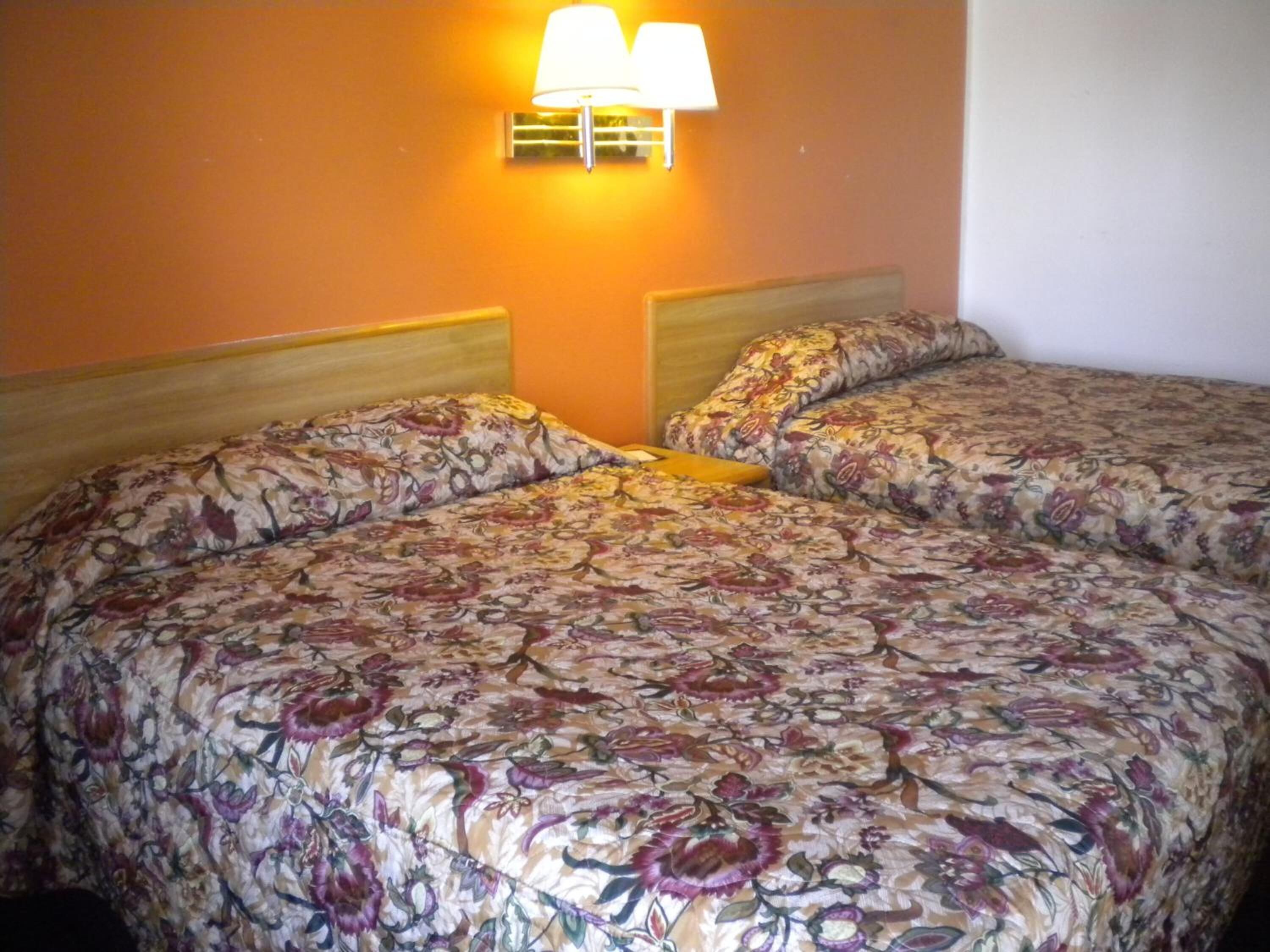 A double bed with floral bedding in a room with orange walls and a wall-mounted lamp.
