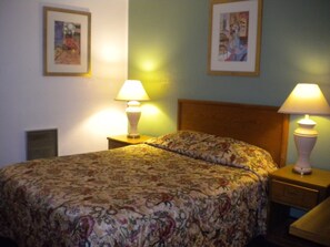 A neatly made bed with floral bedding, two bedside lamps, and framed artwork on the walls.