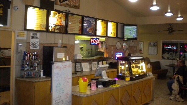 A pizza restaurant interior with a counter, menu boards, and a pizza oven. - Wasco Inn Motel (Wasco)