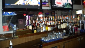 A bar with multiple televisions displaying sports events, a variety of liquor bottles, and glasses on the counter. - Wasco Inn Motel (Wasco)