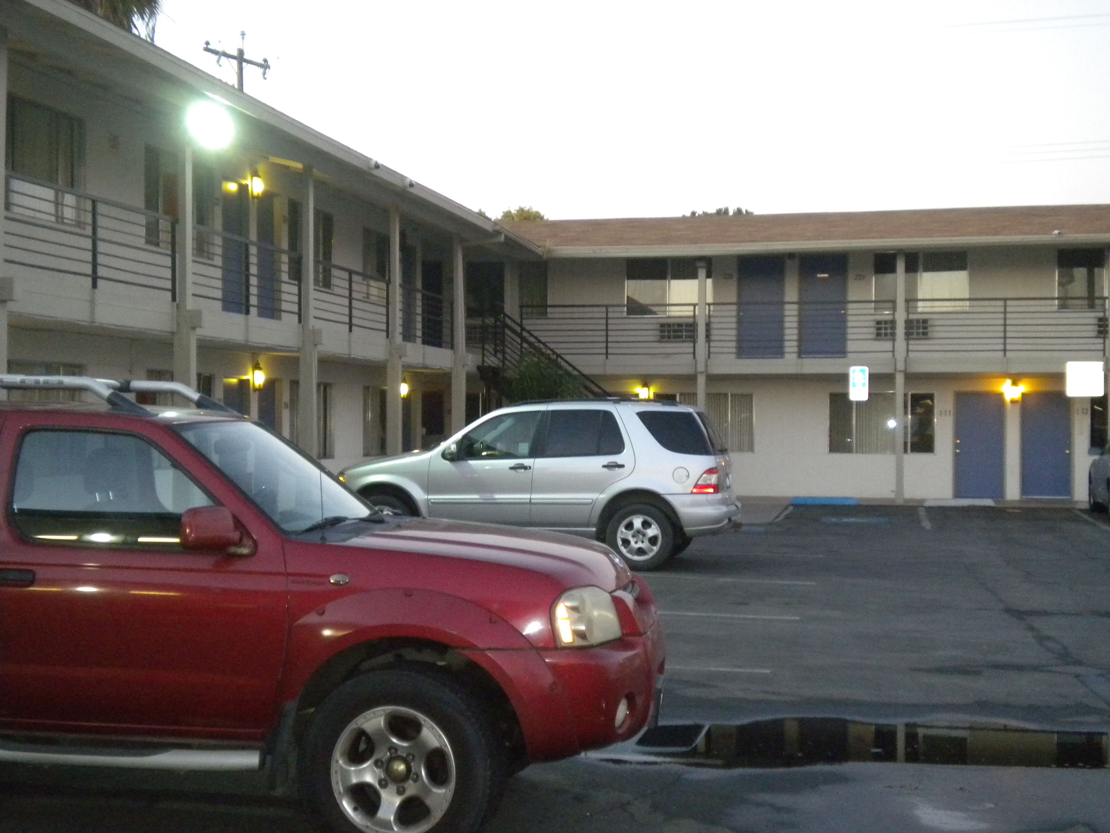 Un estacionamiento con dos coches aparcados frente a un edificio con varias puertas y ventanas.