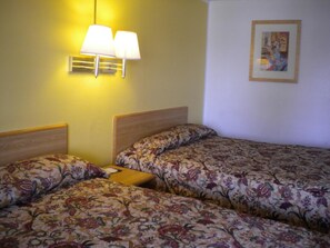 A hotel room with two beds, each with floral-patterned bedding, a bedside table, and a wall-mounted lamp.