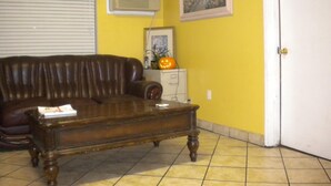 A living room with a brown leather sofa, a wooden coffee table, a white door, and a yellow wall with a framed painting. - Wasco Inn Motel (Wasco)