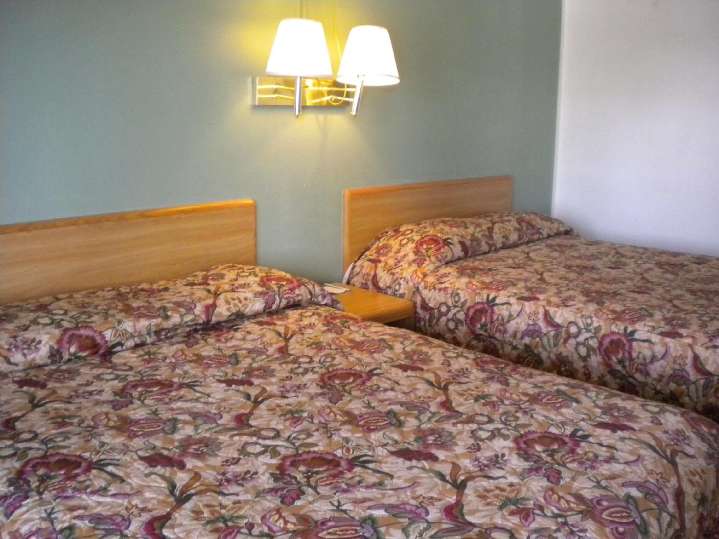 Une chambre avec deux lits, chacun doté de draps à motifs floraux, de têtes de lit en bois et d’un luminaire fixé au mur.