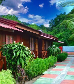 A traditional wooden house with a red roof, surrounded by lush greenery and a paved walkway. - Purnama Beach Resort (Pangkor Island)