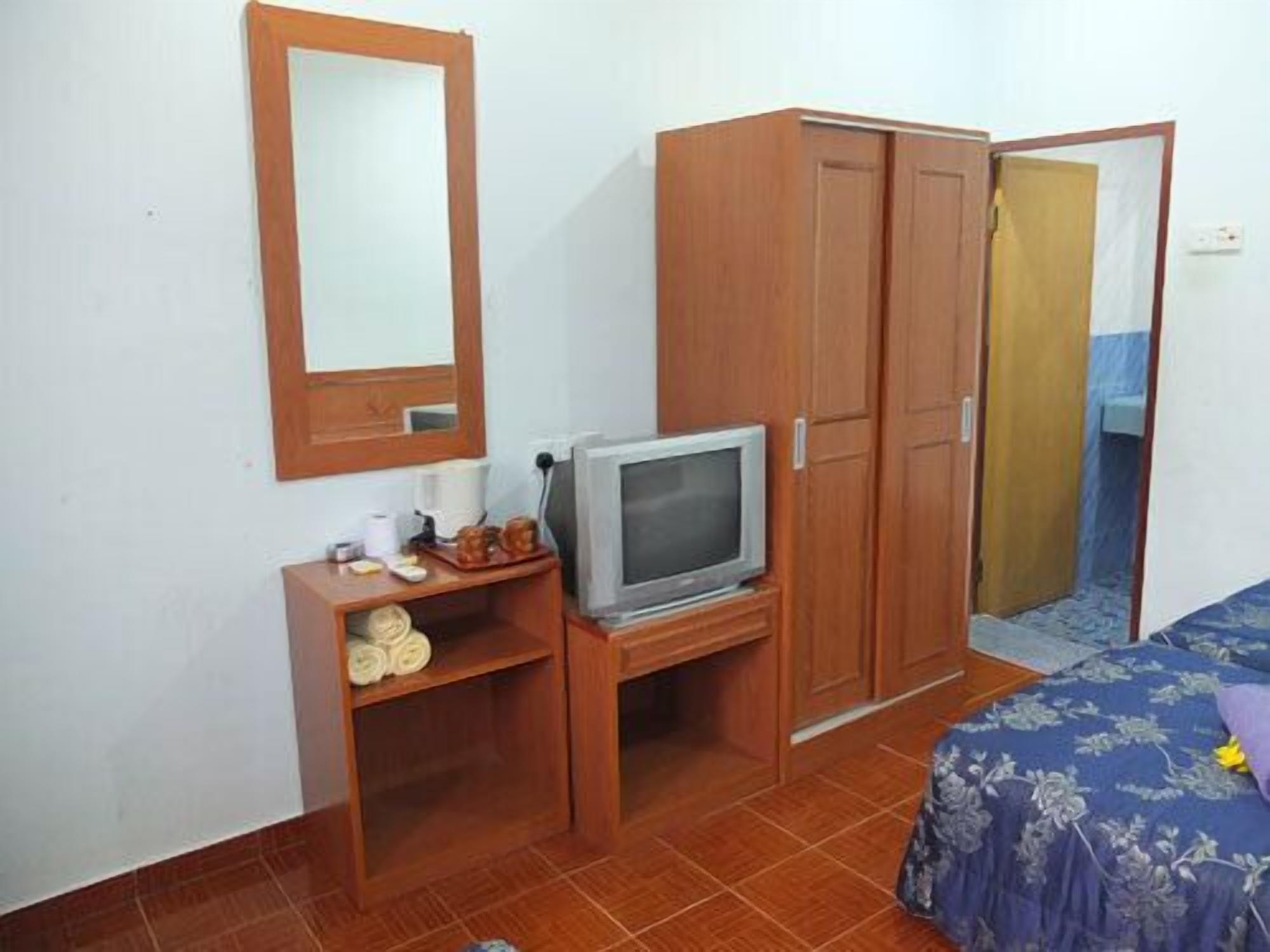 A bedroom with a bed, a TV on a wooden stand, a wardrobe, and a mirror on the wall.