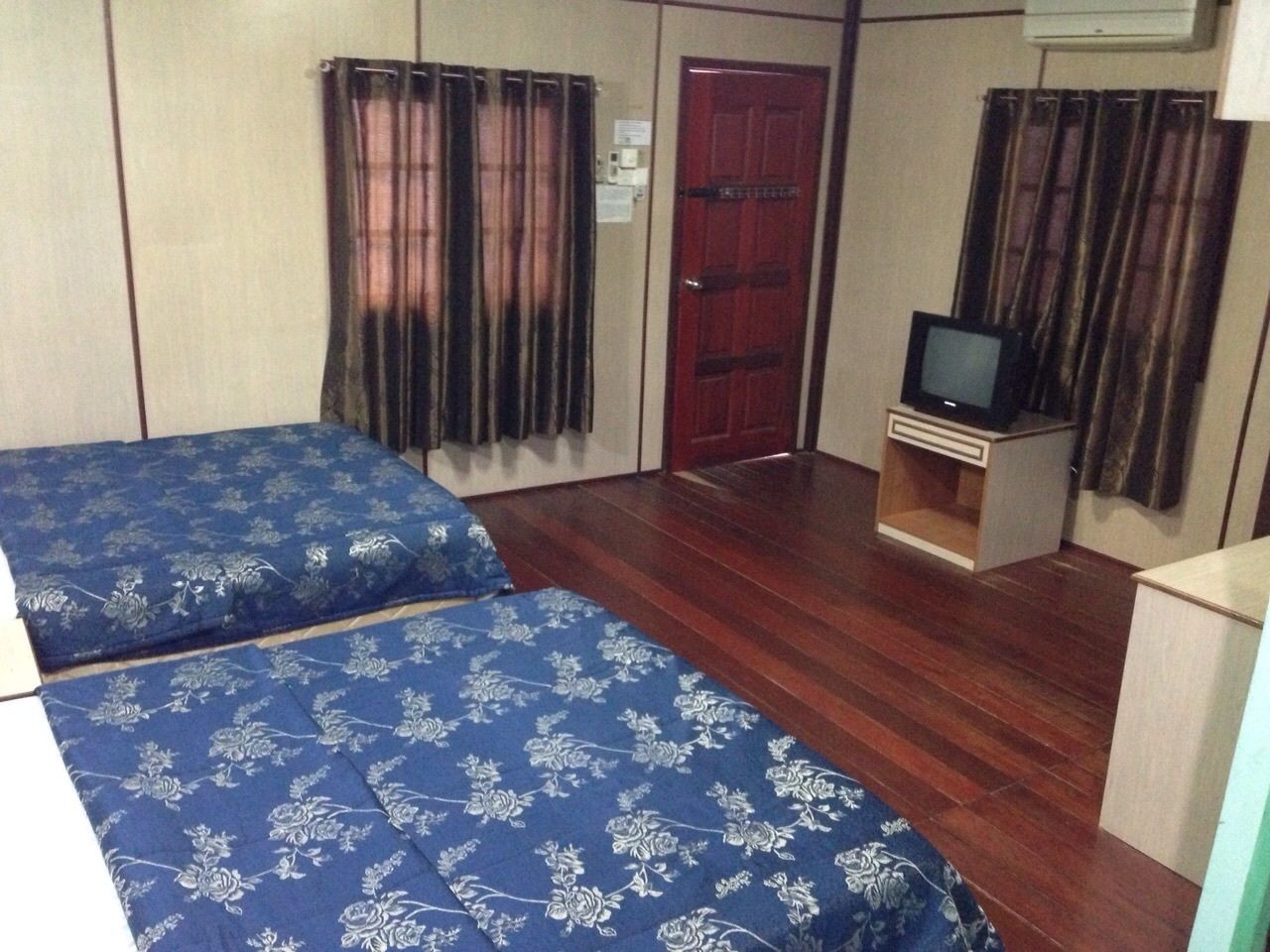 A room with two beds, a television, and a red door.