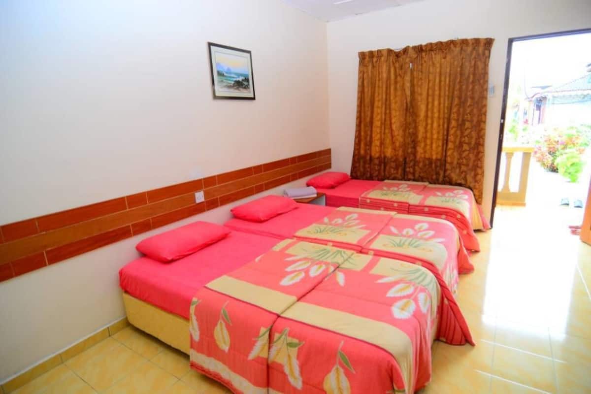 A hotel room with two beds, each with a red and yellow floral bedspread, a brown curtain, and a small framed picture on the wall.