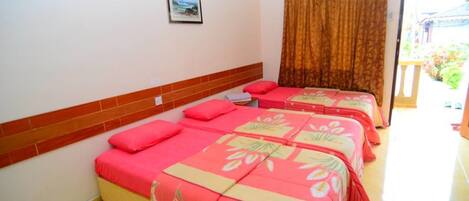A hotel room with two beds, each with a red and yellow floral bedspread, a brown curtain, and a small framed picture on the wall.
