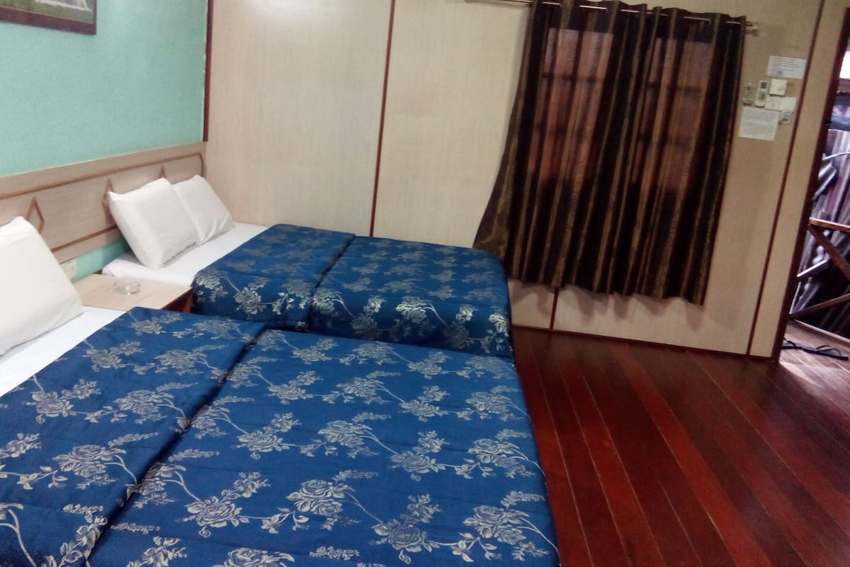 A room with two beds, each with a blue floral bedspread and white pillows. There is a wooden wardrobe and a curtain on the window.