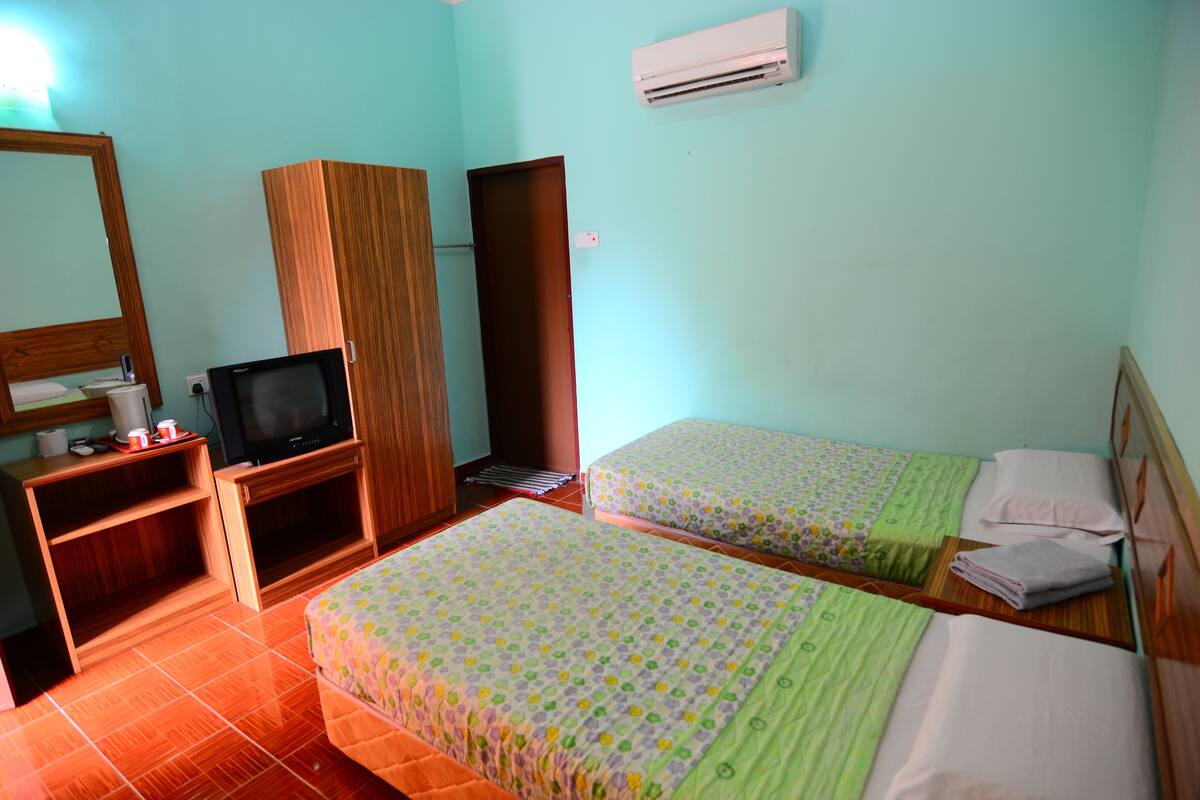 A room with two beds, a television, a wardrobe, and an air conditioning unit.