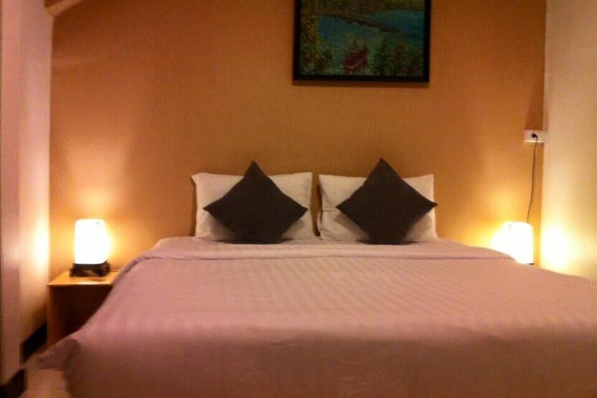 Una habitación de hotel con una cama, dos lámparas de noche y un cuadro en la pared.