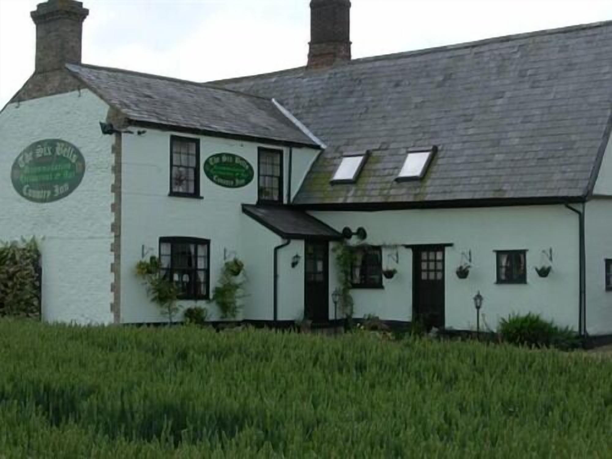A white building with a green sign, a sloped roof, and a small porch area.