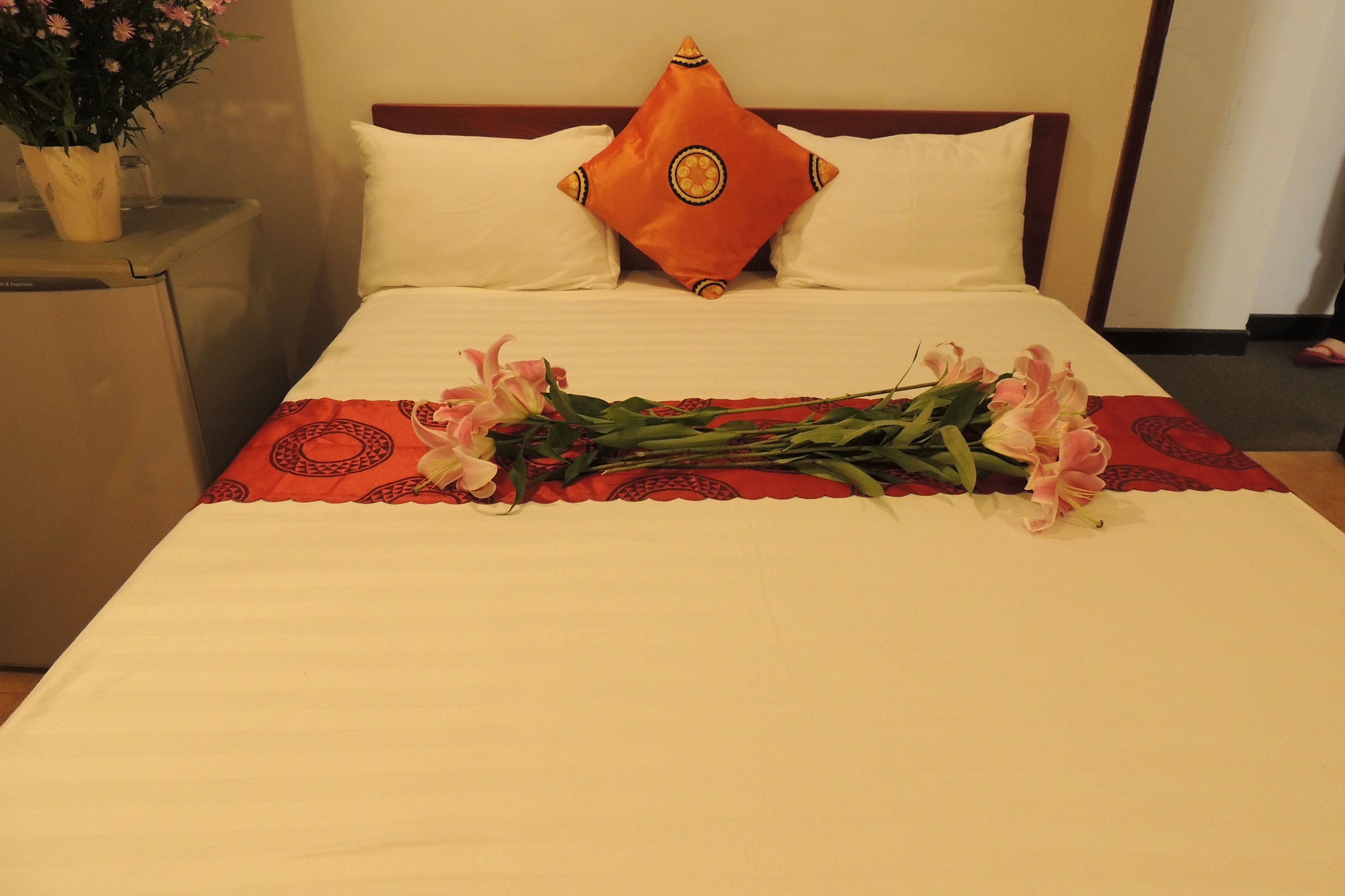 A hotel room with a bed, a nightstand, a potted plant, and a bouquet of flowers.