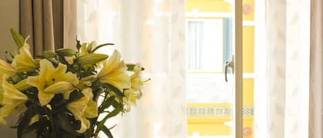A room with a window, a vase with flowers, and a view of a building outside.