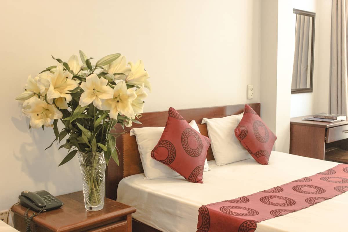 Ein Hotelzimmer mit einem Bett, einer Blumenvase, einem Nachttisch mit Telefon und einem Beistelltisch.