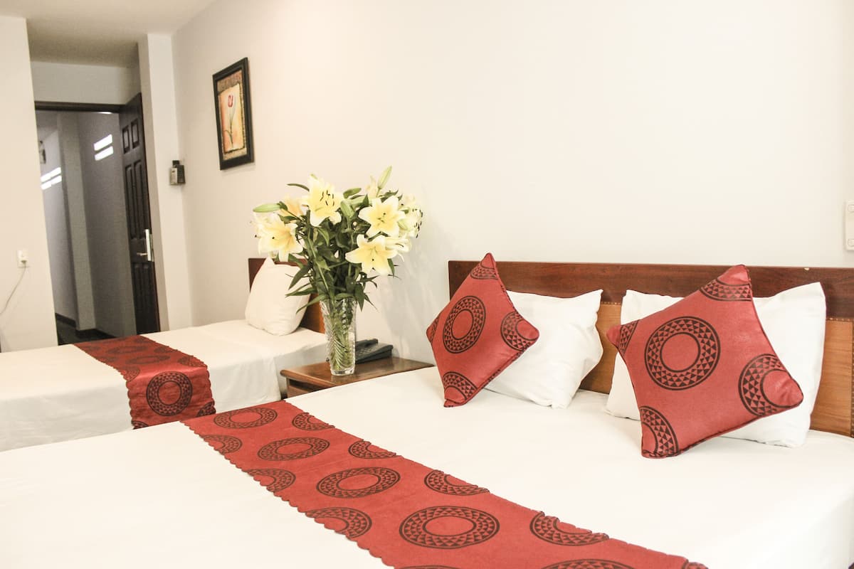 Ein Hotelzimmer mit zwei Betten, einem Blumenstrauß und einem hölzernen Kopfende.