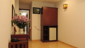 A small room with a wooden cabinet, a refrigerator, a desk with a telephone, and a vase with flowers. - Sao Nam Hotel - Bui Vien Walking Street (Ho Chi Minh City)