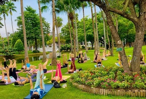 A group of people performing yoga in an outdoor setting with trees and a pond. - Chanaplace Lanna (Chiang Mai)