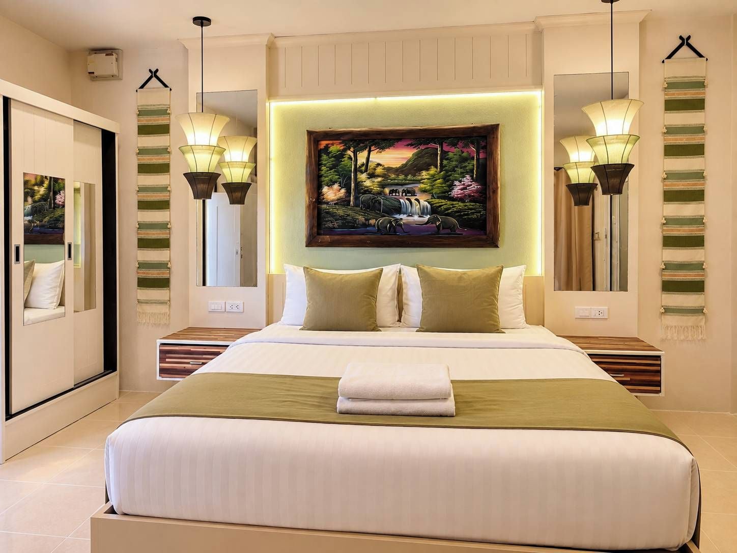 A hotel room with a large bed, a painting above the headboard, and two wall-mounted lamps.