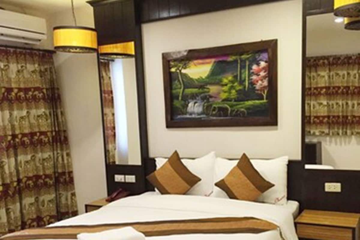 A hotel room with a large bed, a painting on the wall, a fan, and a nightstand.