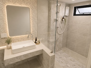 A bathroom with a large mirror, a sink, a shower, and a window.