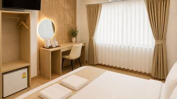 Quarto de hotel com cama, escrivaninha, cadeira, televisão, espelho e janela com cortinas.