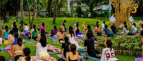 Eine Gruppe Menschen praktiziert Yoga auf Matten in einem Park mit Bäumen und einer dekorativen goldenen Struktur.