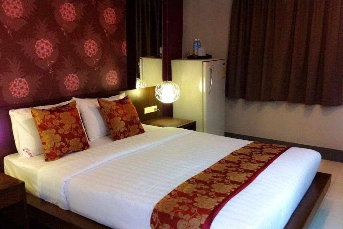 A hotel room with a bed, nightstand, lamp, and curtains.