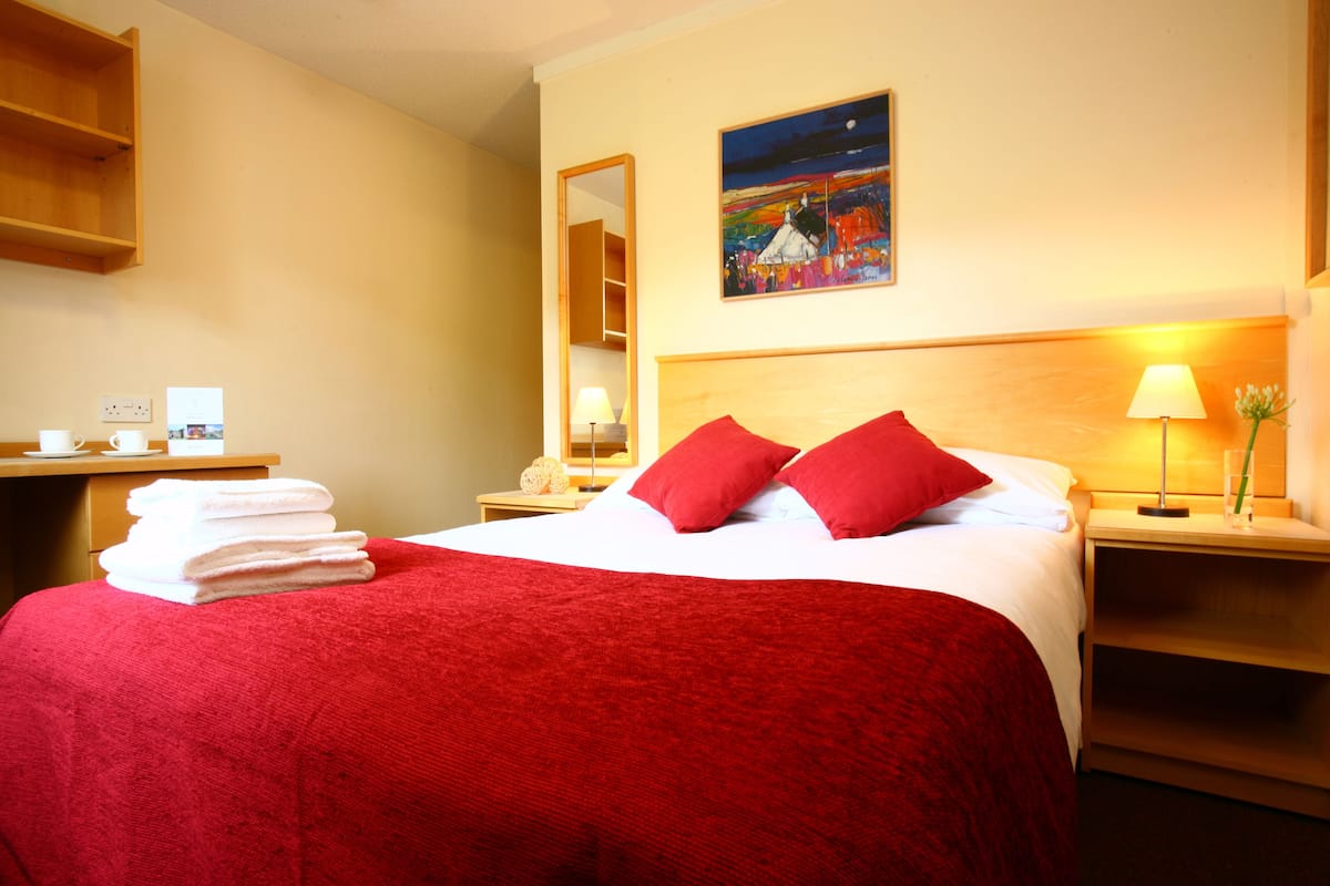 Une chambre d’hôtel avec un lit, une table de chevet, une lampe, un miroir et un tableau au mur.