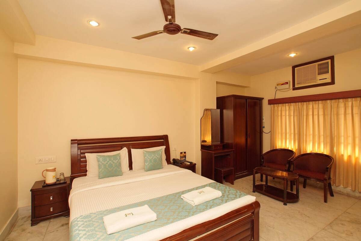 A hotel room with a bed, a nightstand, a desk, a chair, a ceiling fan, and a window with curtains.