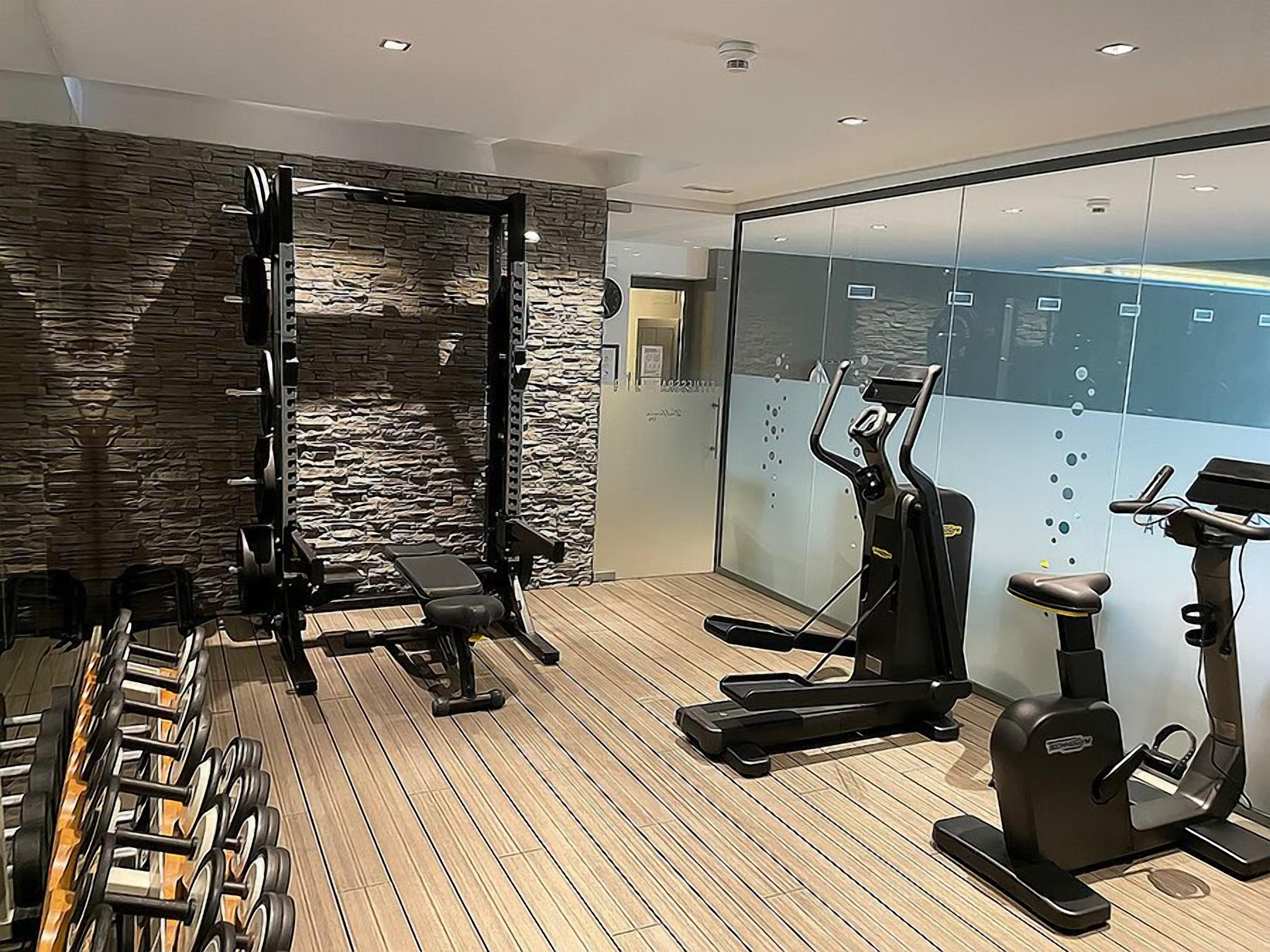 Ein modernes Fitnessstudio mit Steinwand, unterschiedlicher Trainingsausstattung und einem großen Fenster.