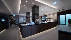 Een moderne hotel lobby met een centraal gelegen receptie, een zithoek met sofa’s en een groot raam met uitzicht op de stad.