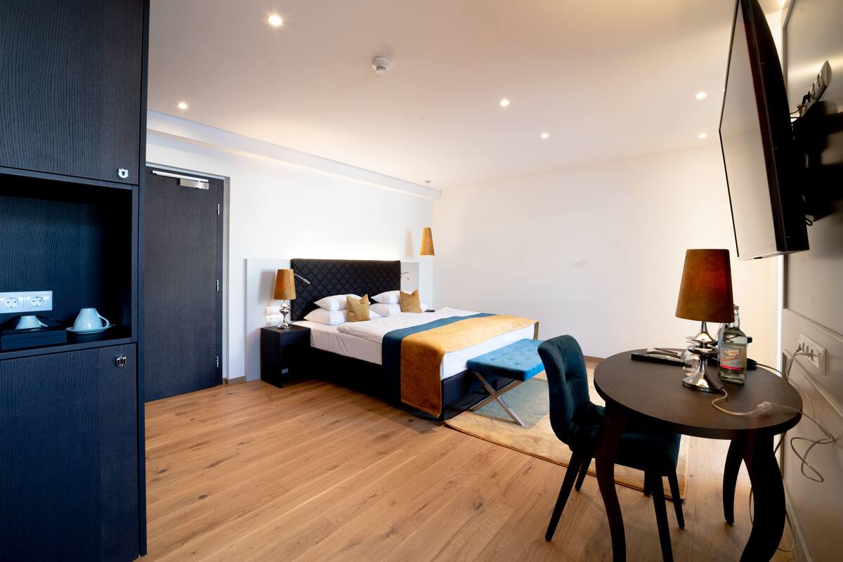 Una habitación de hotel moderna con cama, mesita de noche, lámpara y una pequeña mesa de comedor.