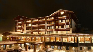 Een meerhoog hotel in traditionele Alpenstijl, met balkons en een overdekt terras met zitplaatsen.