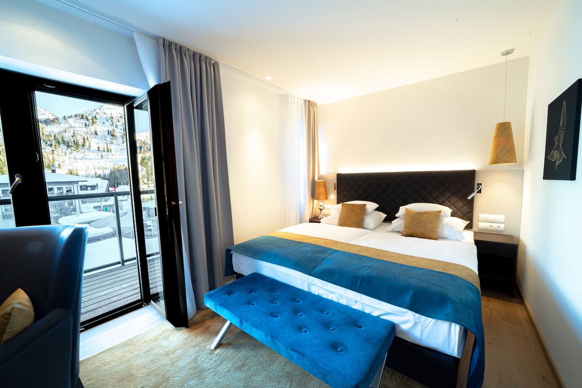 Habitación de hotel con una cama grande, un banco, una silla, una mesita de noche y vistas a un paisaje nevado a través de una puerta corrediza.