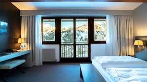 Een hotelkamer met een bed, een bureau, een stoel, een raam met gordijnen en uitzicht op een besneeuwde berg.