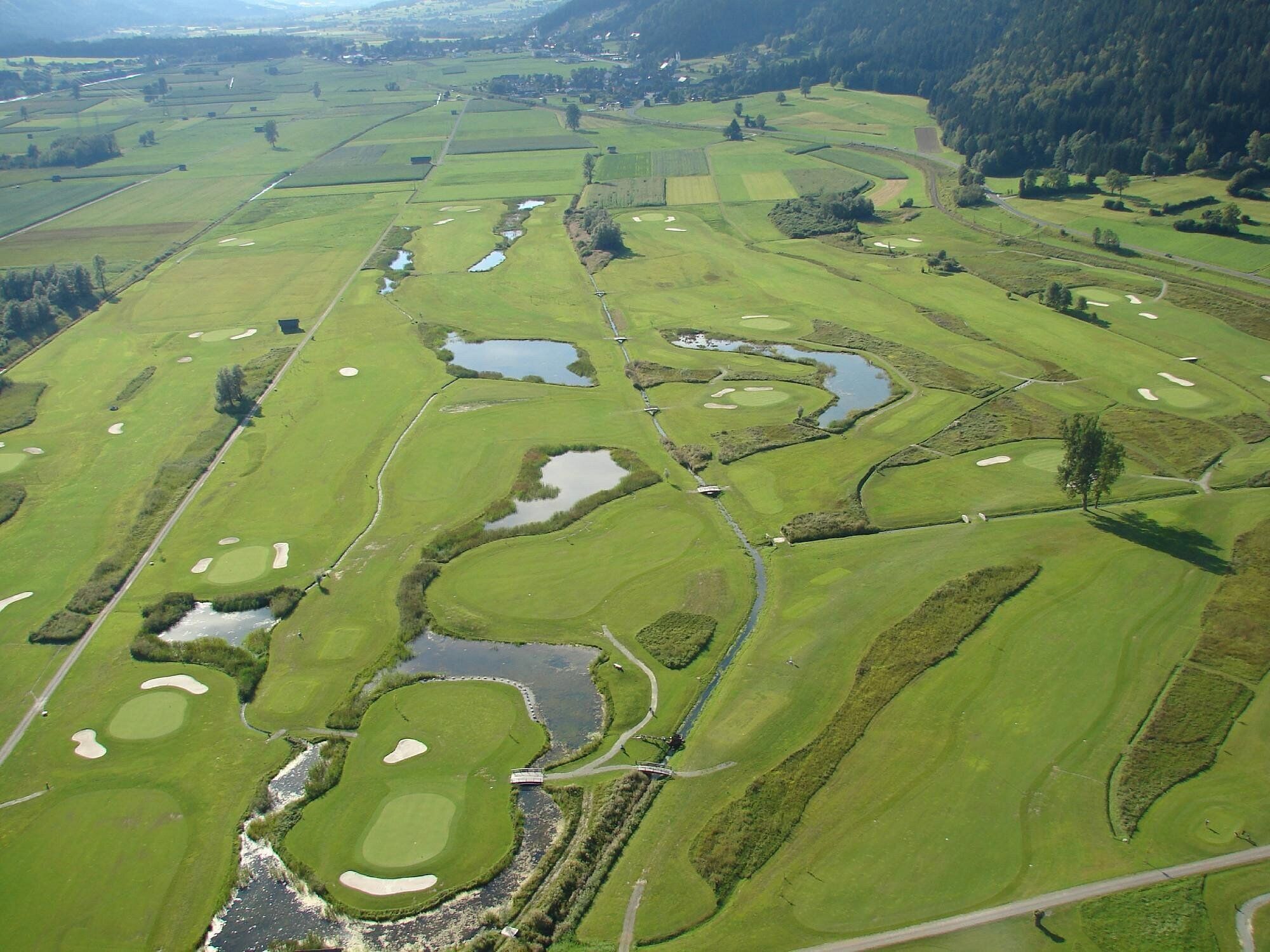 Un campo de golf con varios hoyos, obstáculos acuáticos y un club de campo.