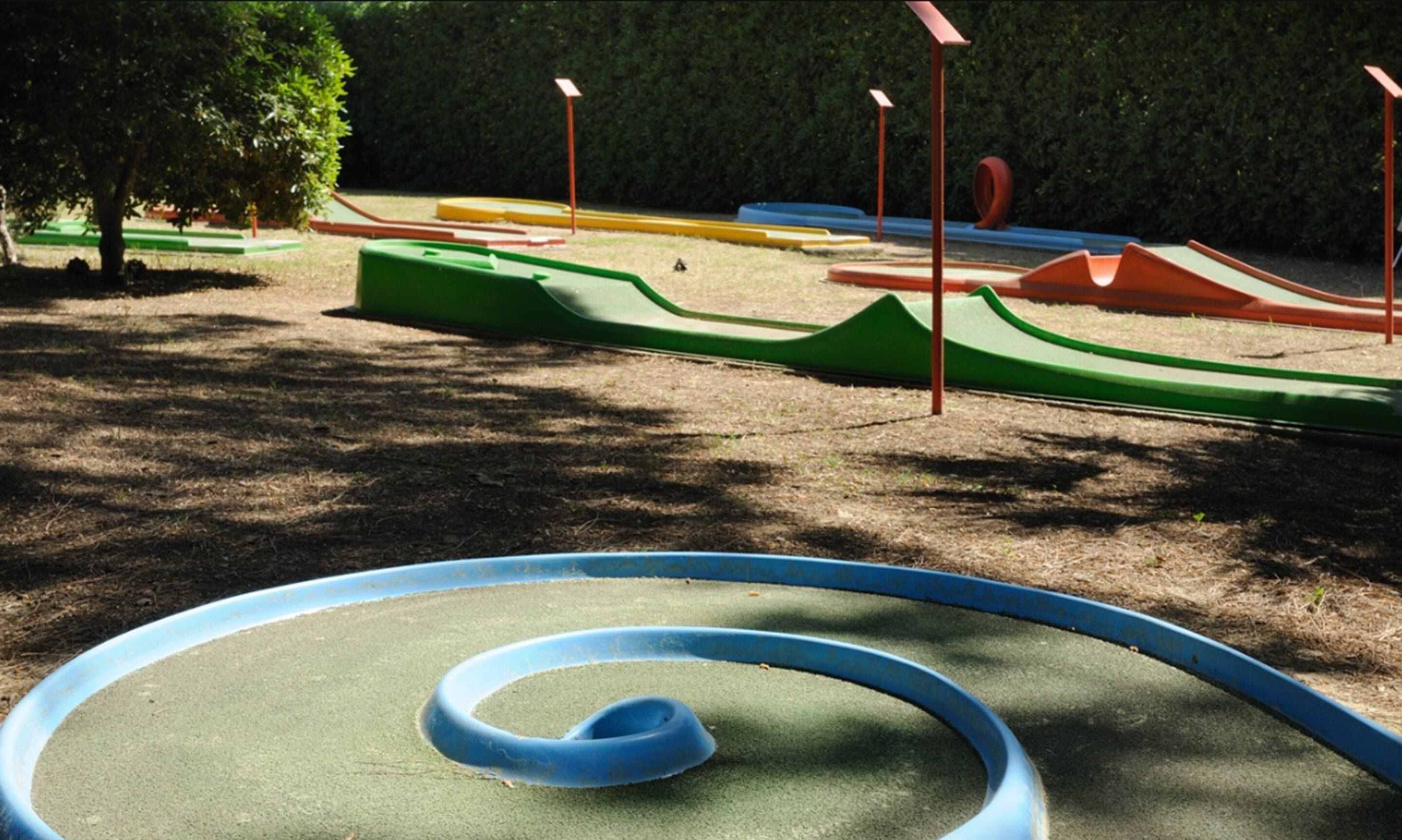 Un parque infantil con diversas estructuras de juego, incluyendo un tobogán espiral azul, toboganes verdes y rojos, y zonas de escalada amarillas y azules.