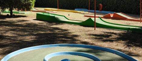 Un parque infantil con diversas estructuras de juego, incluyendo un tobogán espiral azul, toboganes verdes y rojos, y zonas de escalada amarillas y azules.