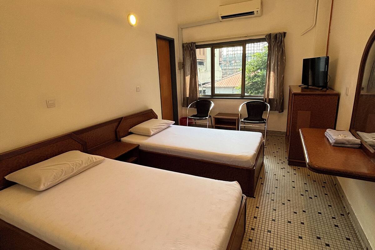 A hotel room with two beds, a desk with a TV, a ceiling fan, and a window with curtains.