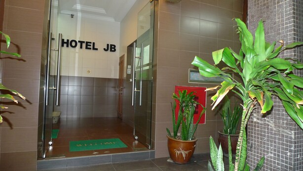 A hotel entrance with a glass door, a welcome mat, and potted plants. - Hotel J.B. (Johor Bahru)