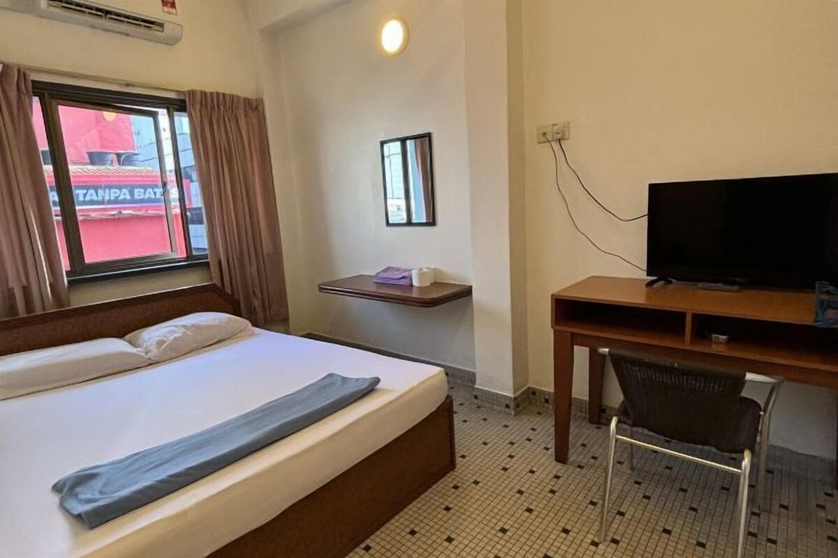 A hotel room with a bed, a desk, a chair, a television, and a window with curtains.