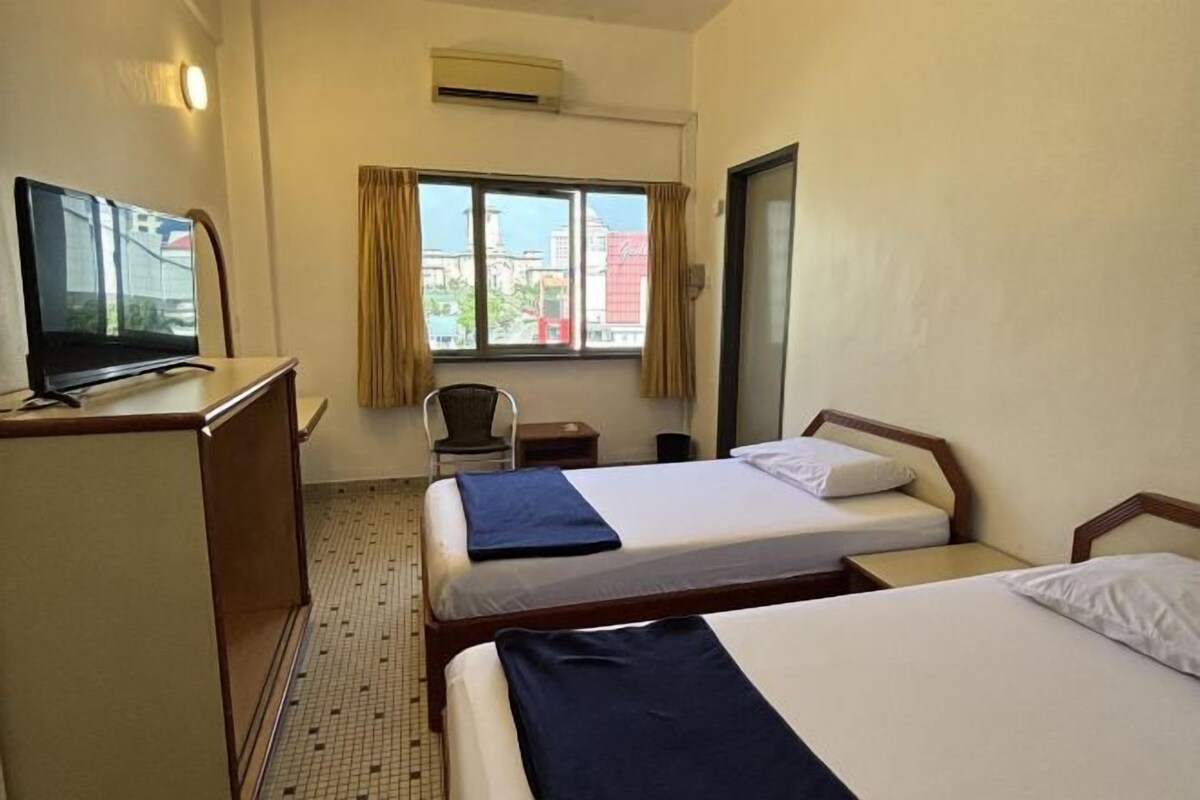 A hotel room with two beds, a desk, a chair, a TV, and a window with curtains.