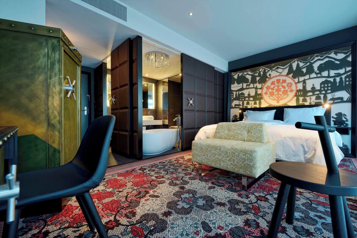 A hotel room with a bed, a chair, a desk, a large mirror, and a decorative wall.