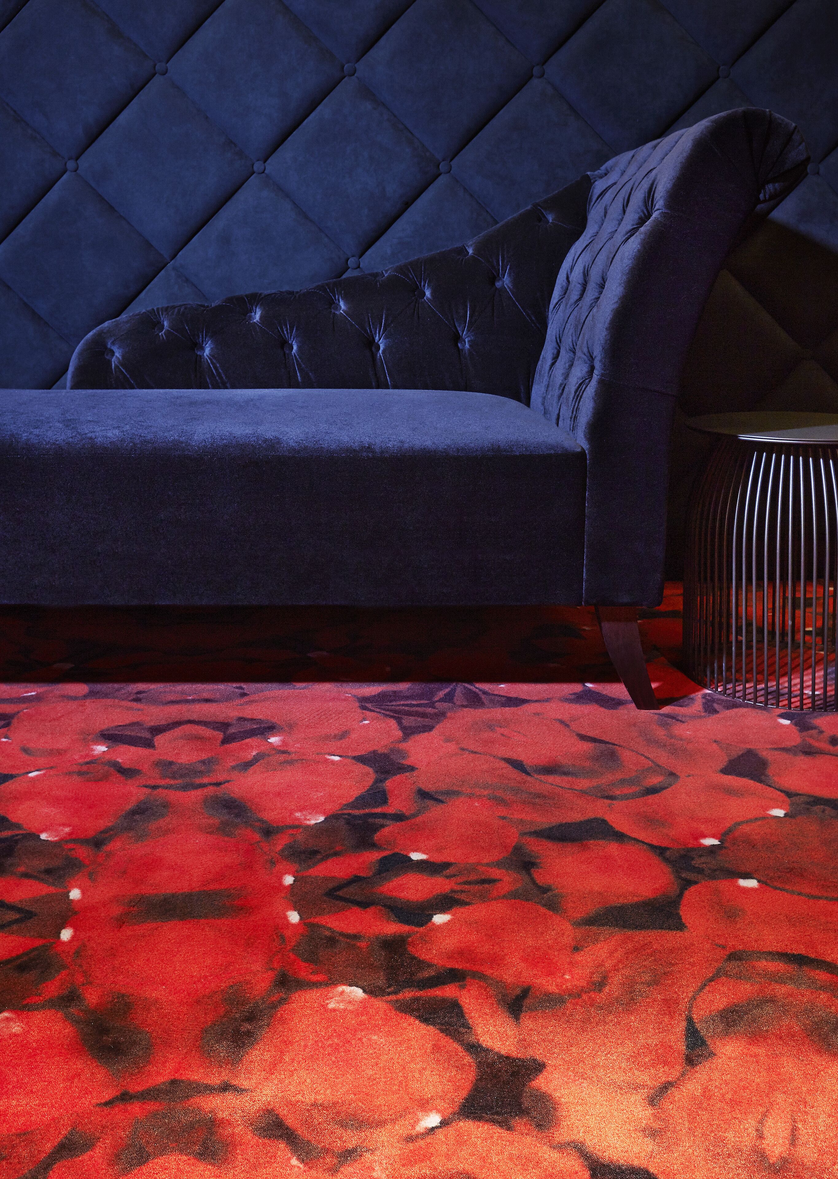 A dark blue sofa with a tufted backrest, positioned on a red patterned carpet.
